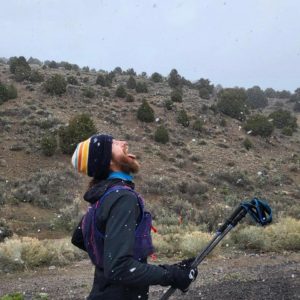 Man catches snowflakes in his mouth as he runs past a hill with trees