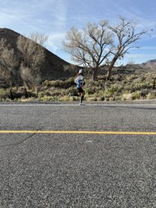 Man runs on road with tree in background. Shoes are strung from tree. 