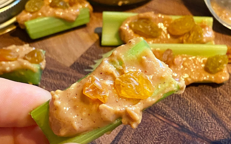 Fingers holding pieces of celery with peanut butter spread