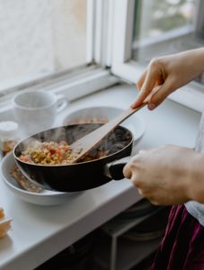 hands cook meal in pan over plate in white kitchen