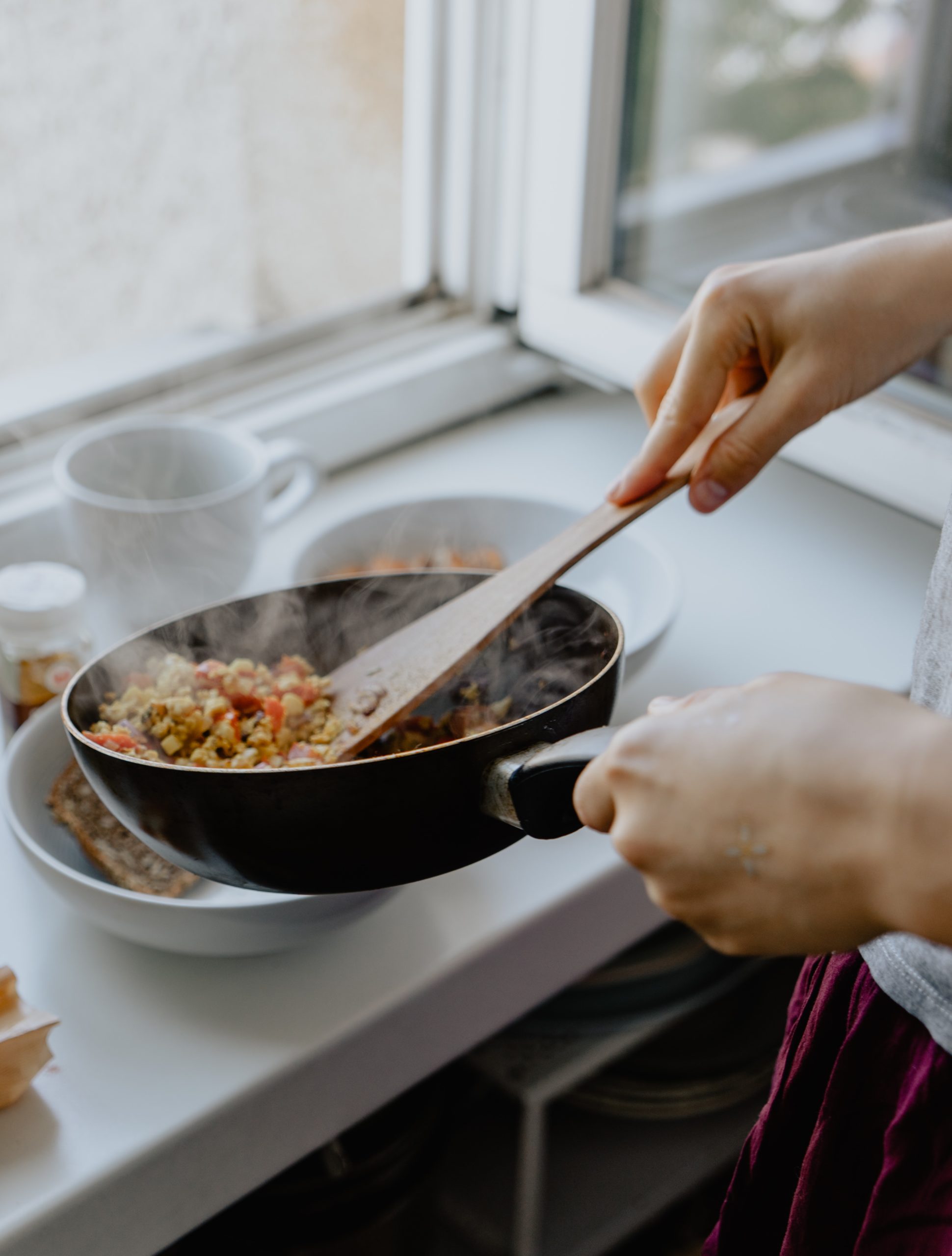 hands cook meal in pan over plate in white kitchen