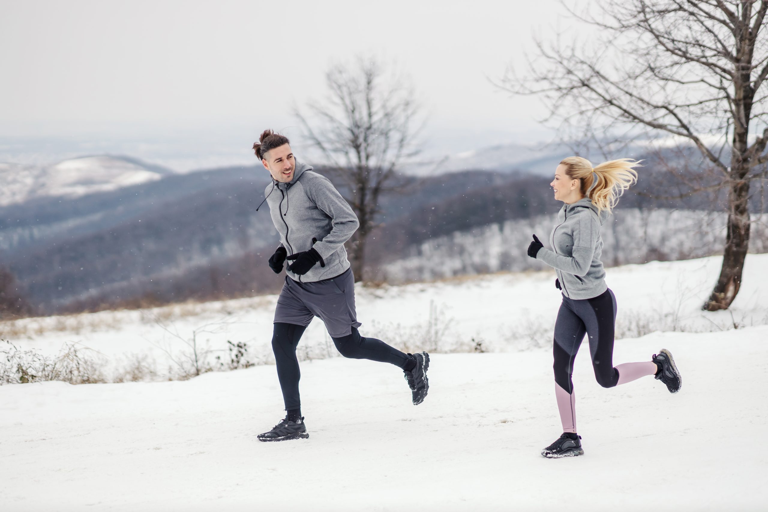 Two runners are out on their cold-weather winter run. They're smiling and enjoying the snowy landscape. Build healthy winter habits that go beyond performace!