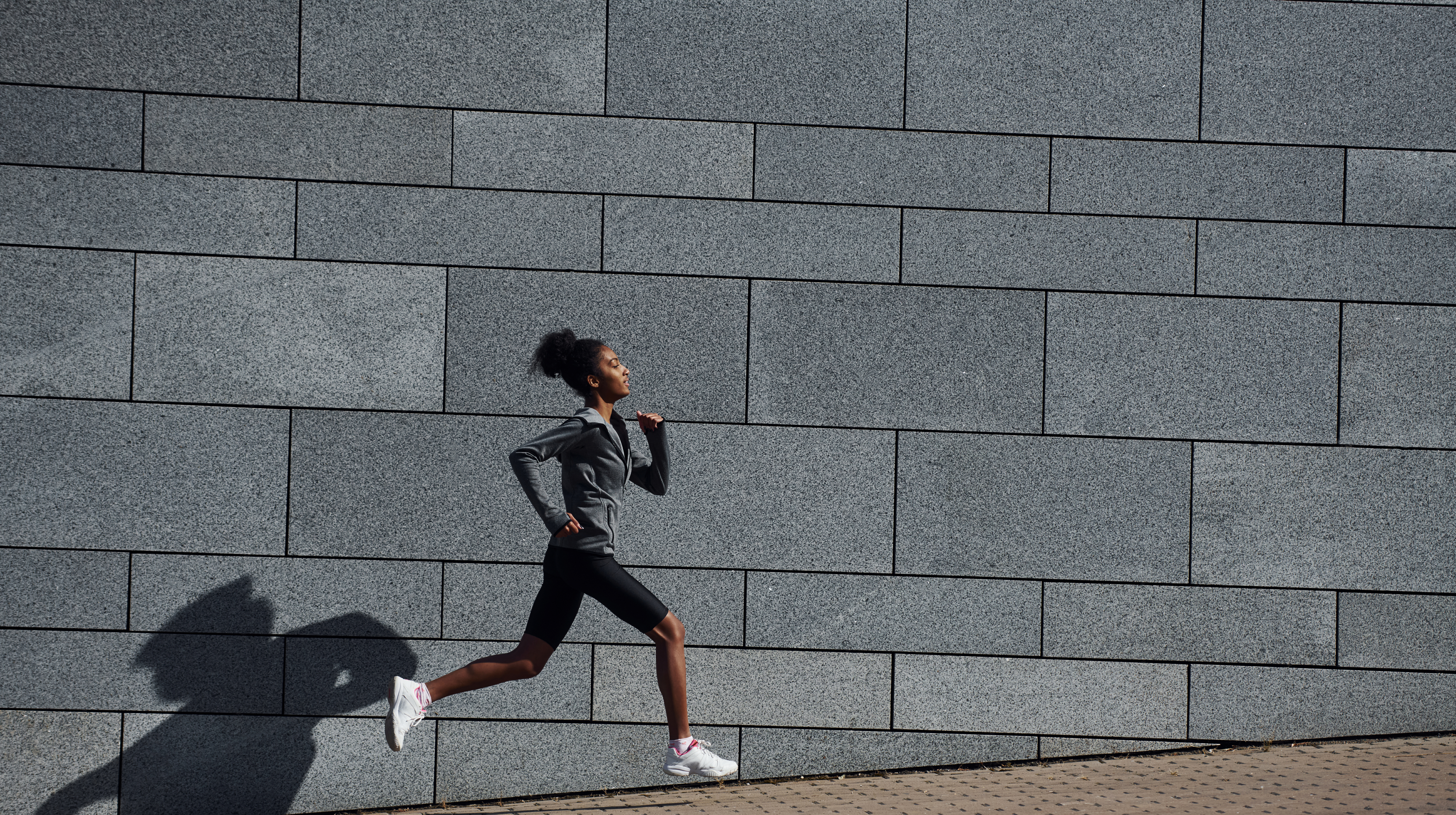 Urban running: a woman in athletic clothes sprints in an urban environment.
