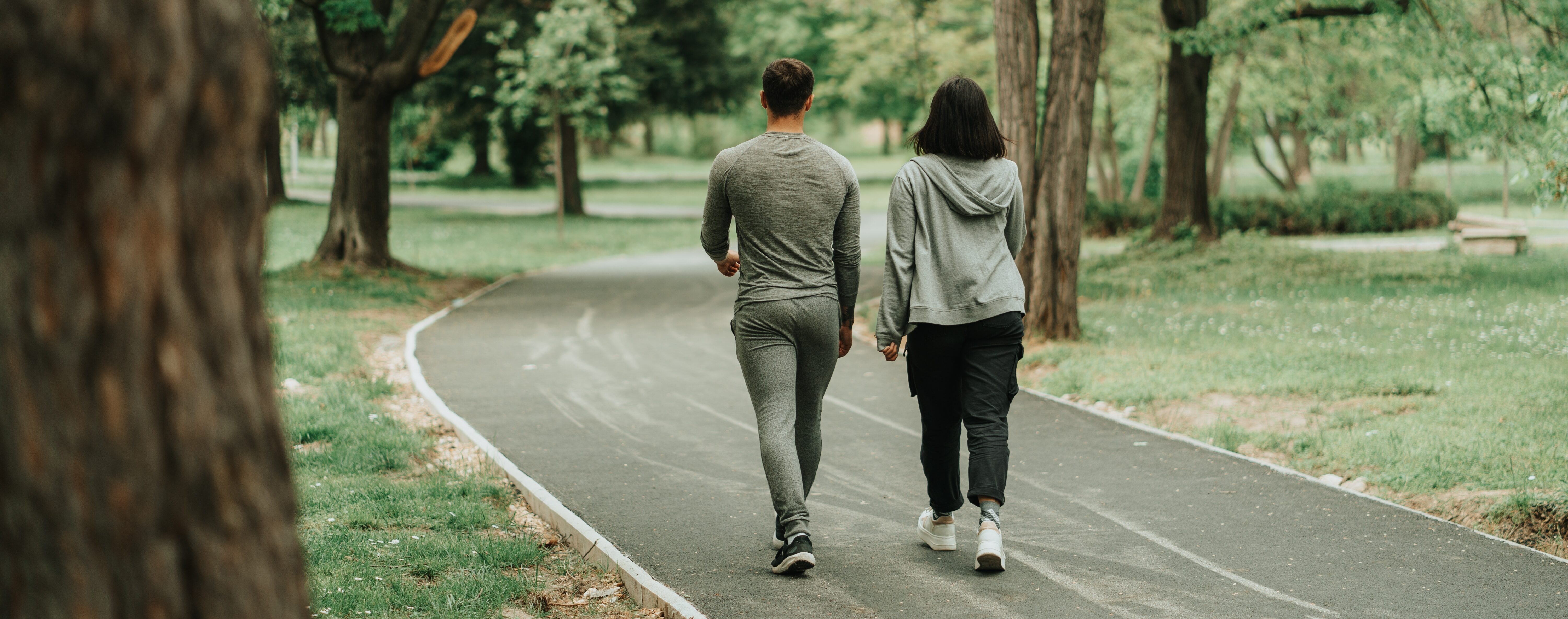 Two people do walk training on a park path, surrounded by greenery.
