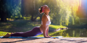 A young woman does yoga, a great cross training for runners, on the side of a lake on a sunny day