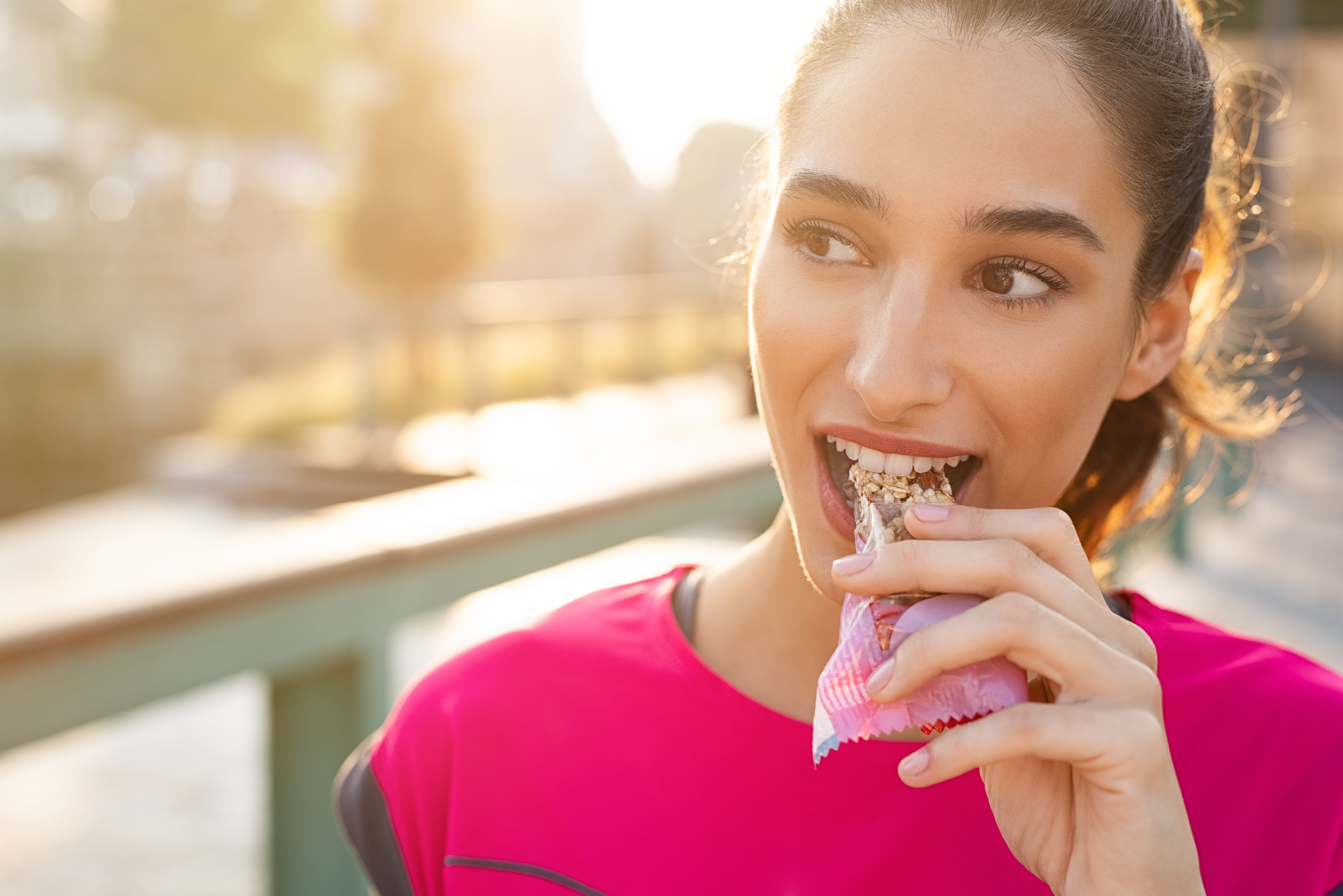 An athletic woman in a pink top eats a bar mid-run; what GMOs can be in the bar? What are the GMO facts and fiction?