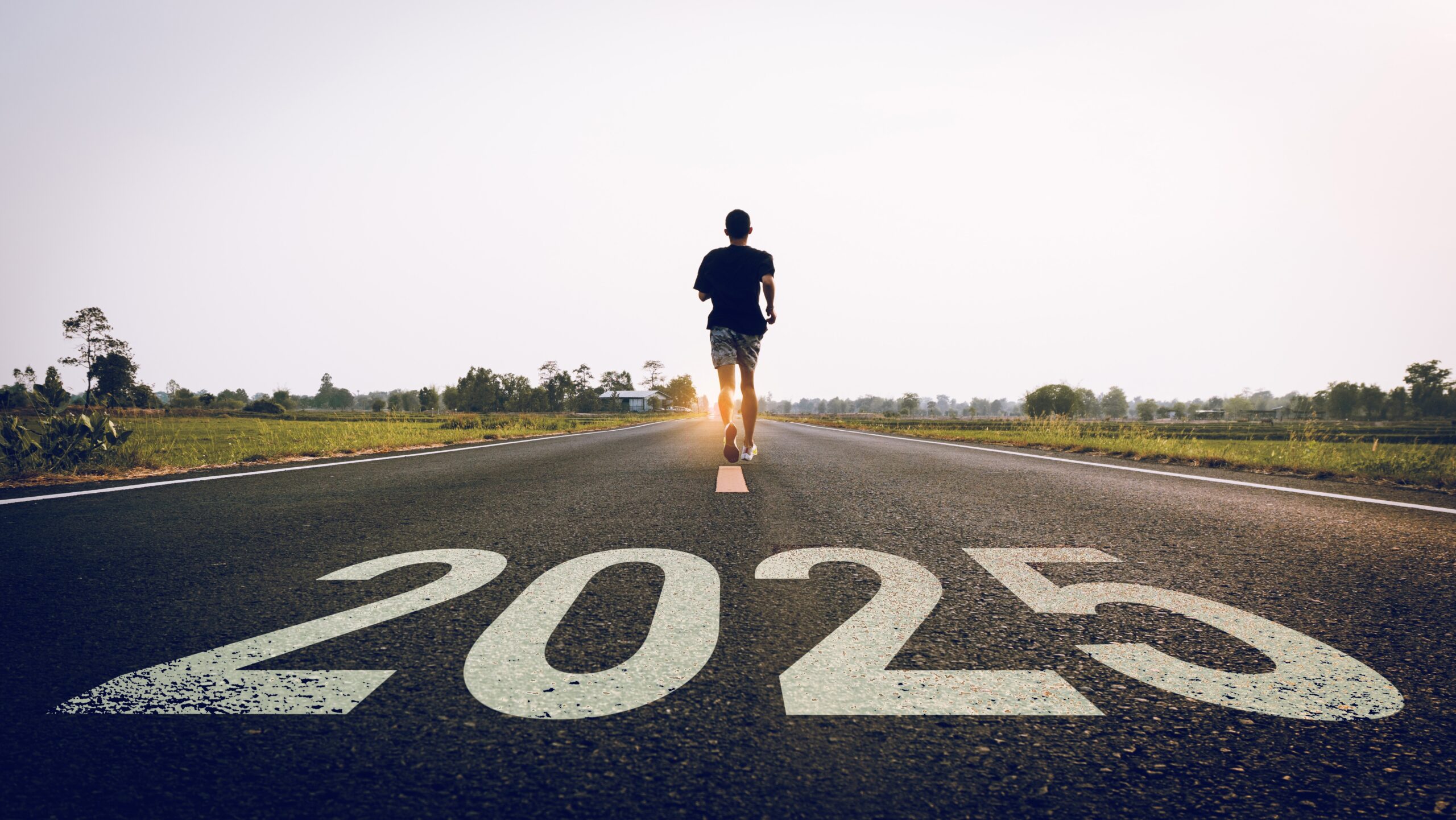 A runner is running across and away from a 2025 sign on a road, running towards the rising sun, starting work on his New Year Goals