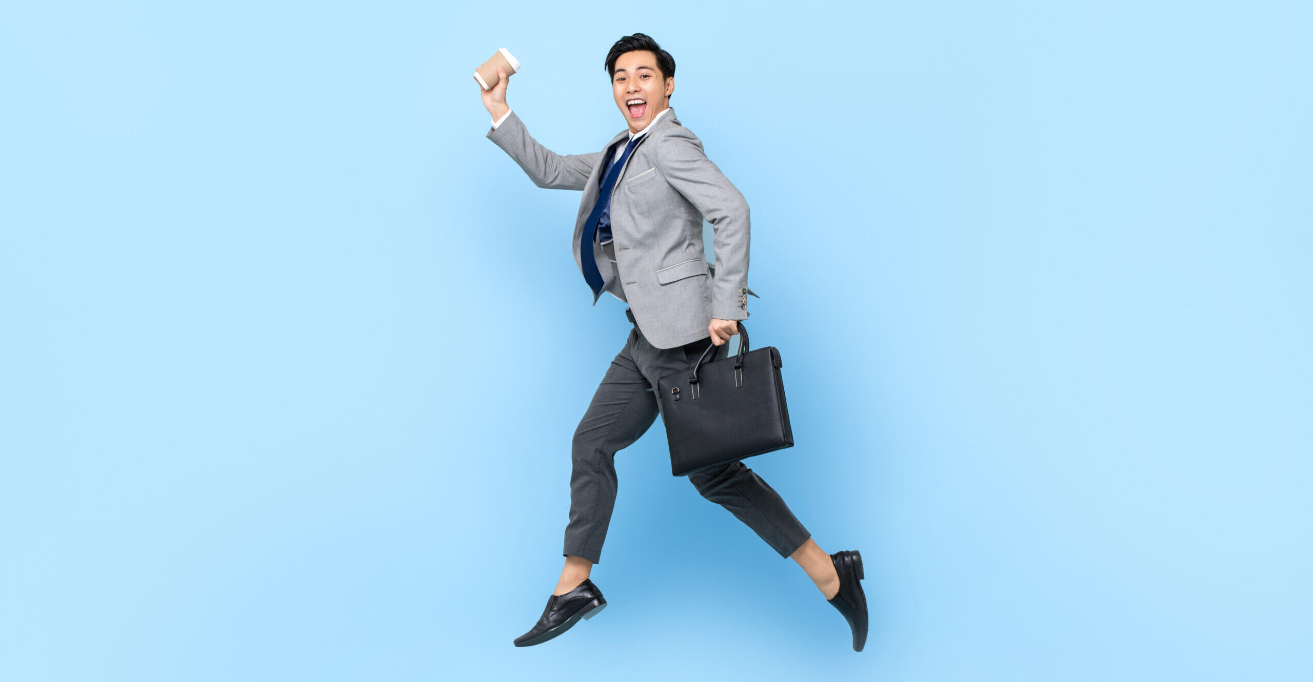 A young professional businessman with a smile runs with a suitcase and coffee.