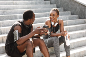 A Black man and woman sit on the stair during their training session and chat, combining their marathon training and social life