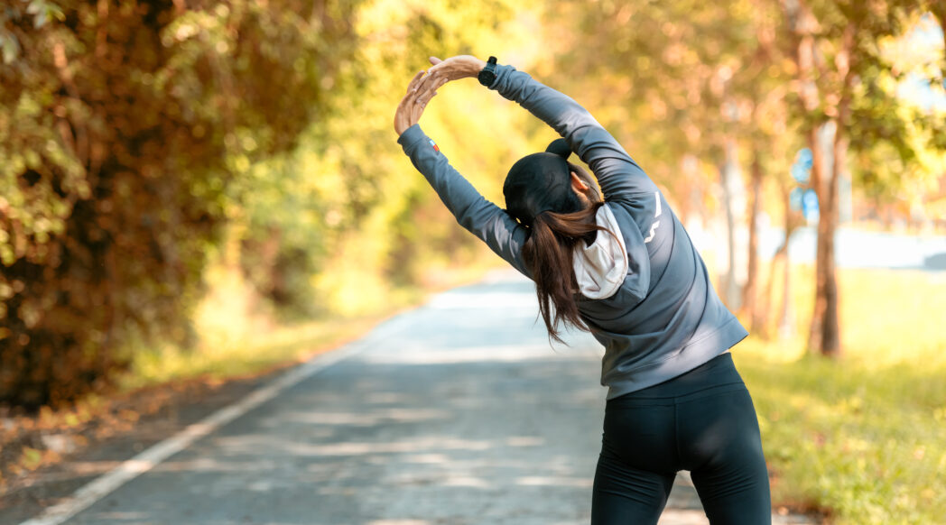 A woman runner takes a break from running and stretches with autumn leaves in the background
