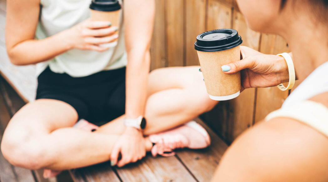 A close-up of two runners taking a break, sitting down, and enjoying a cup of coffee and running.