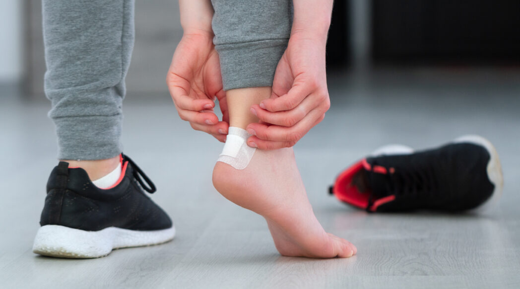 A runners is taping a blister on the heel of their foot.