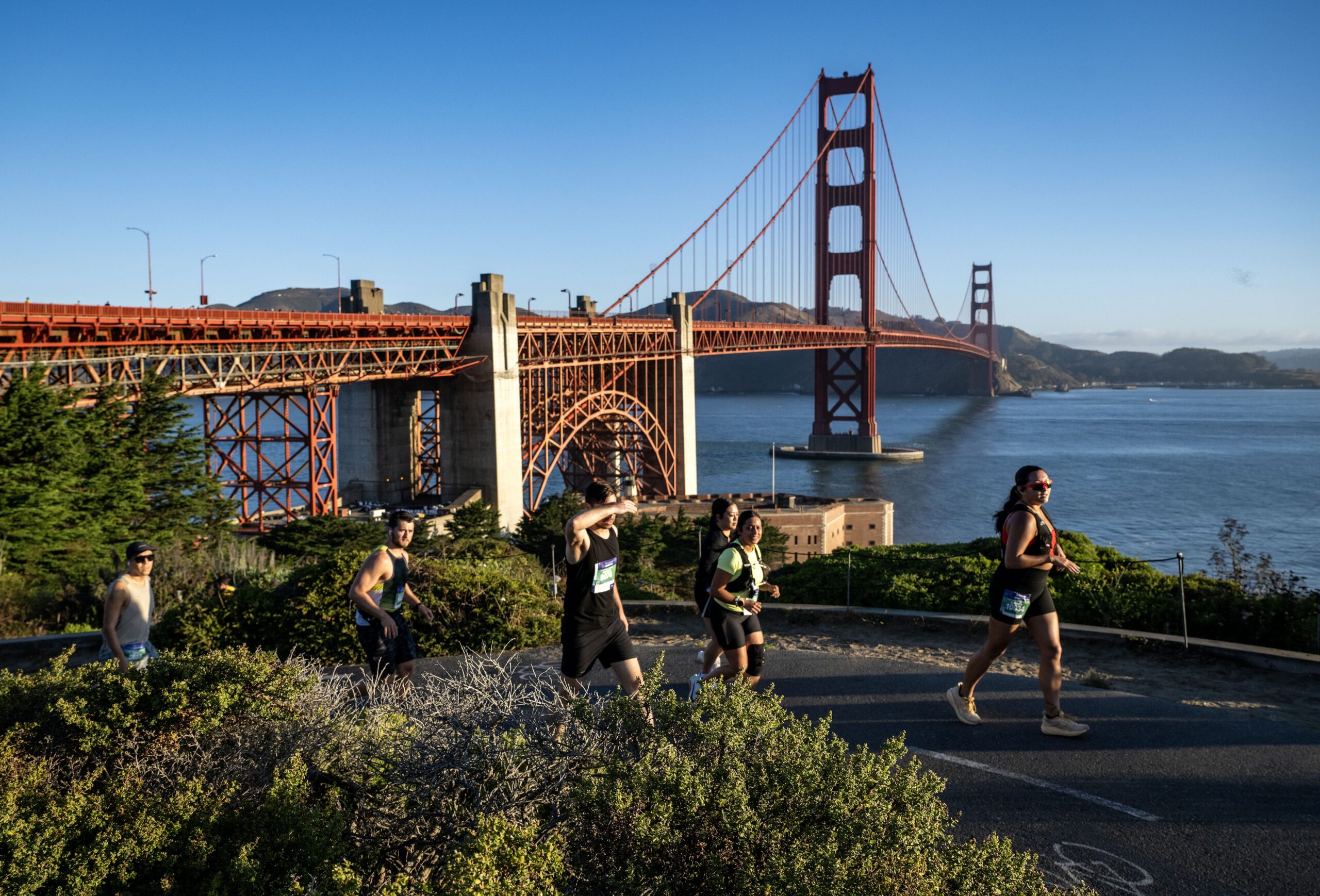 The Golden Gate Bridge, one of the Golden Gate Dozen, with small silhoutettes of runners running in front of it