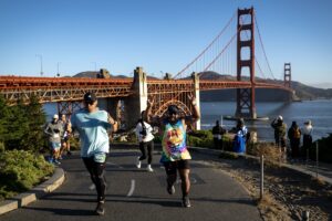 Two runners run and jump in celebration in front of the Golden Gate Bridge
