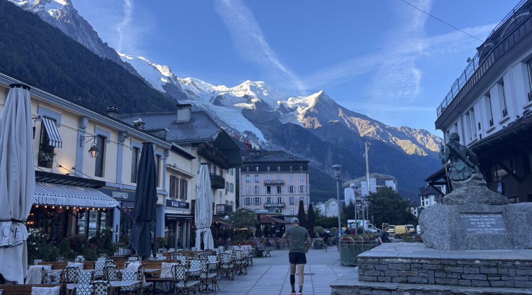A lone runner in the early morning hours runs through the centre of Chamonix during UTMB week, with Mont Blanc in the background. European running Culture.